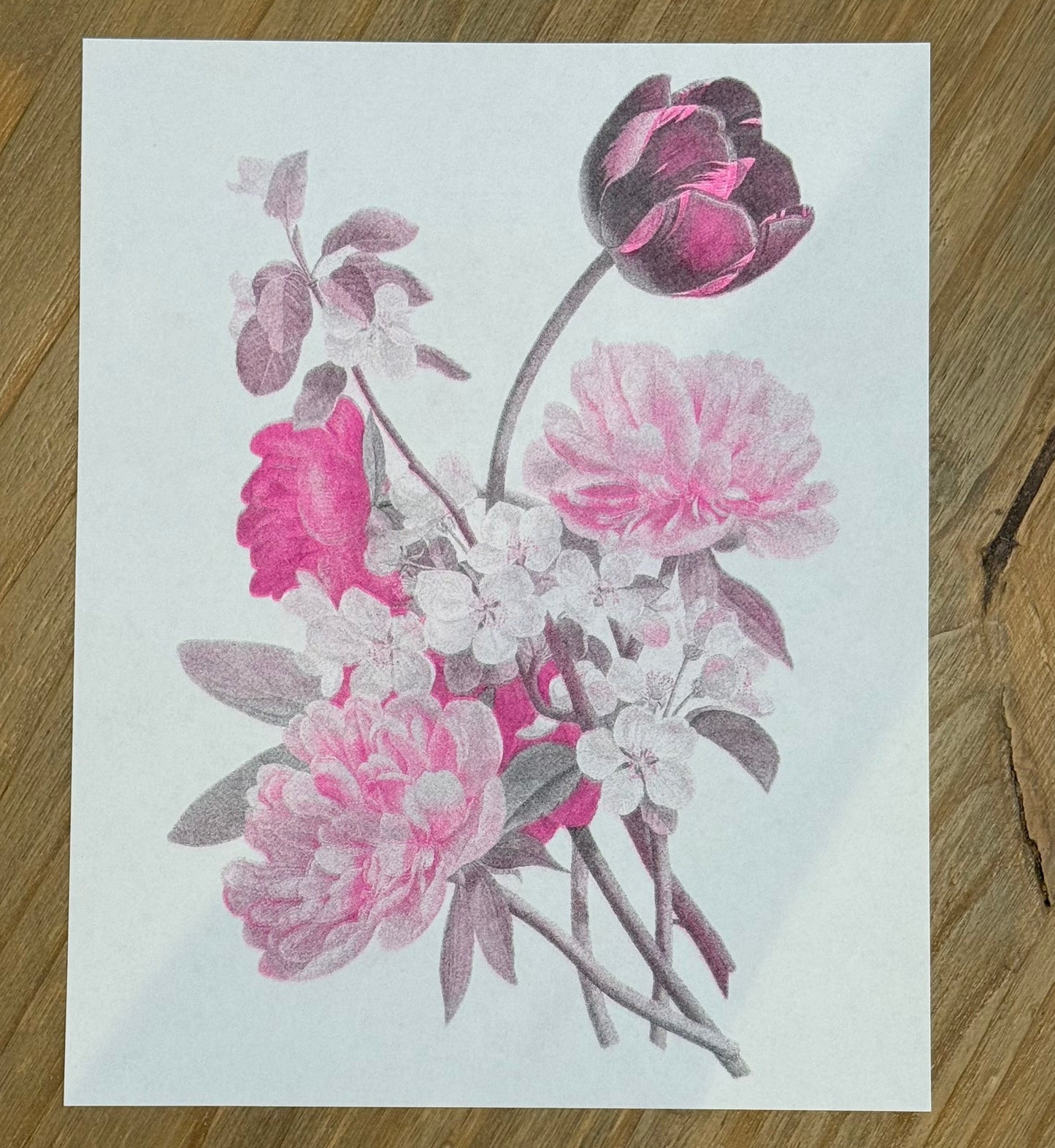 Floral design on a white card with pink and purple flowers, placed on a wooden surface.