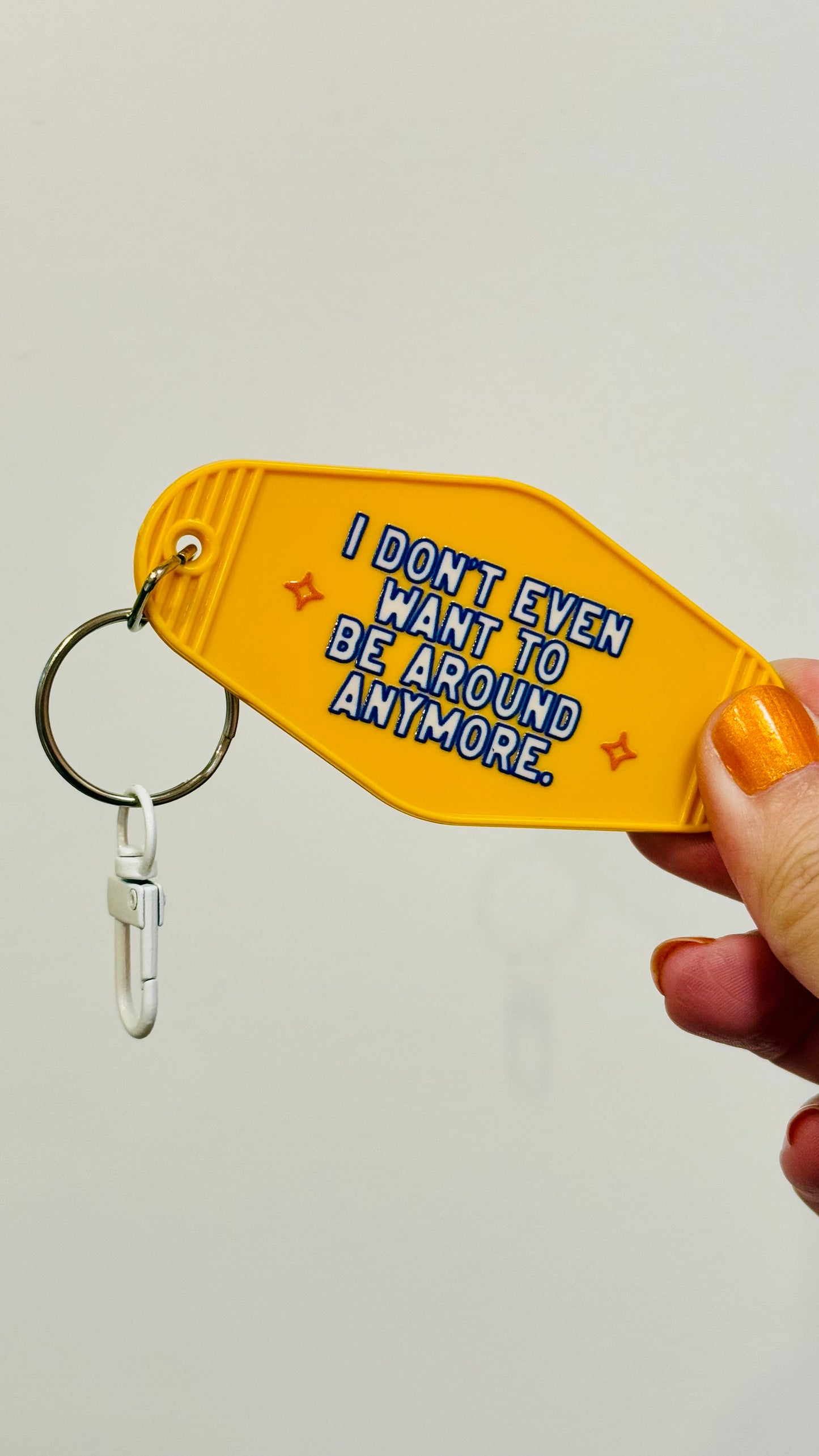 Yellow keychain with text 'I don't even want to be around anymore' held by a hand against a light gray background
