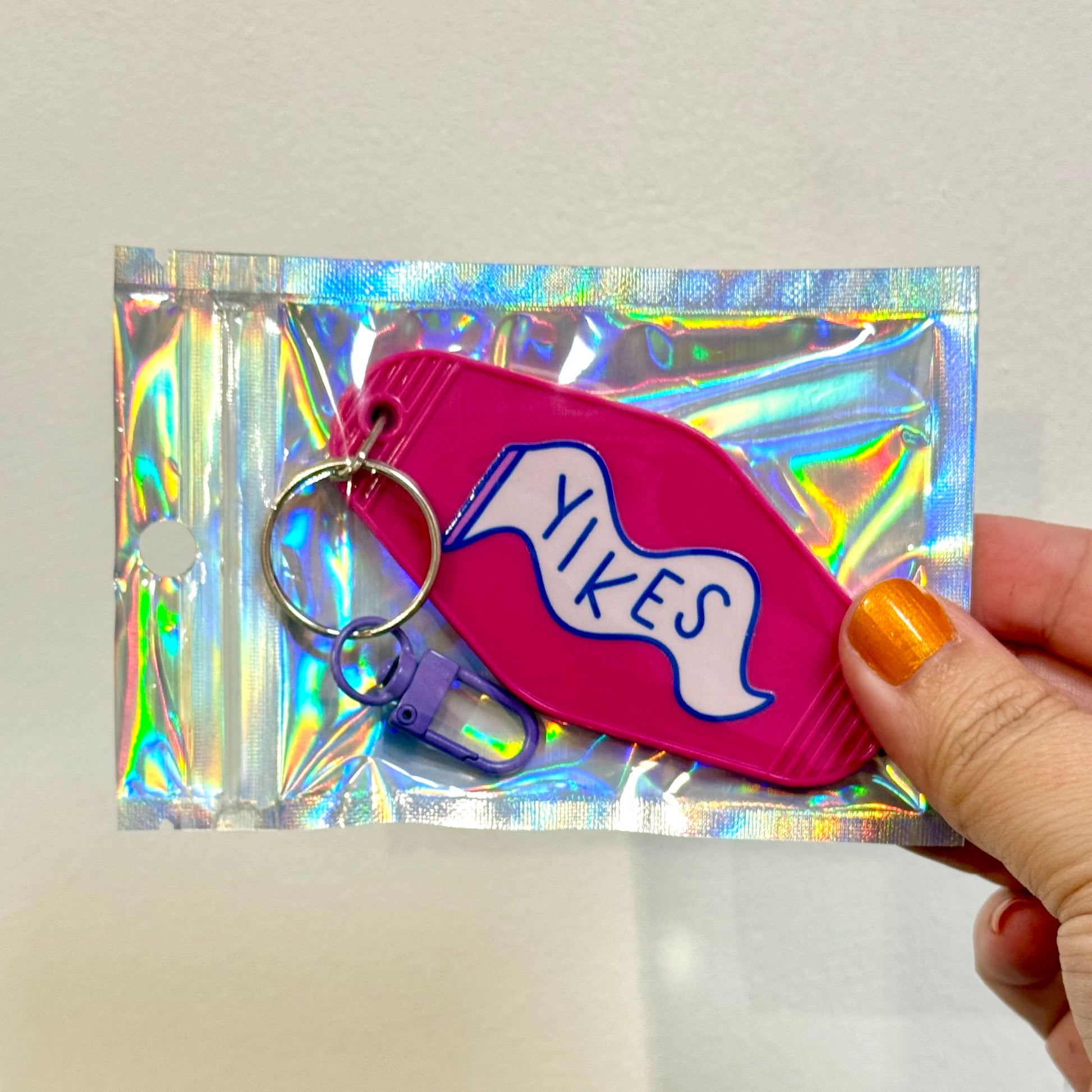 Pink keychain with 'Yikes' text held over a reflective silver background