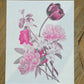Floral design on a white card with pink and purple flowers, placed on a wooden surface.