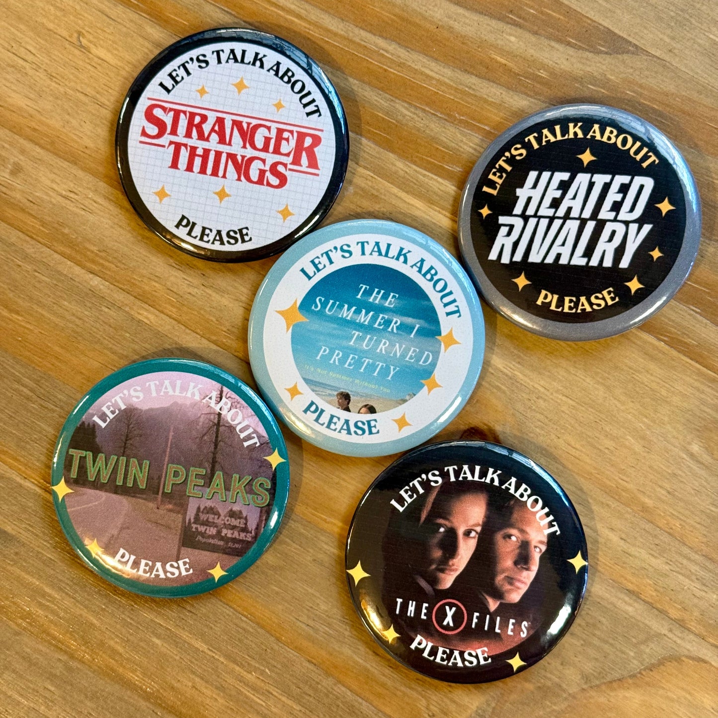 Five buttons with TV show references on a wooden surface