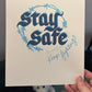 Hand holding a print with 'Stay Safe, Keep Fighting' text on a neutral background